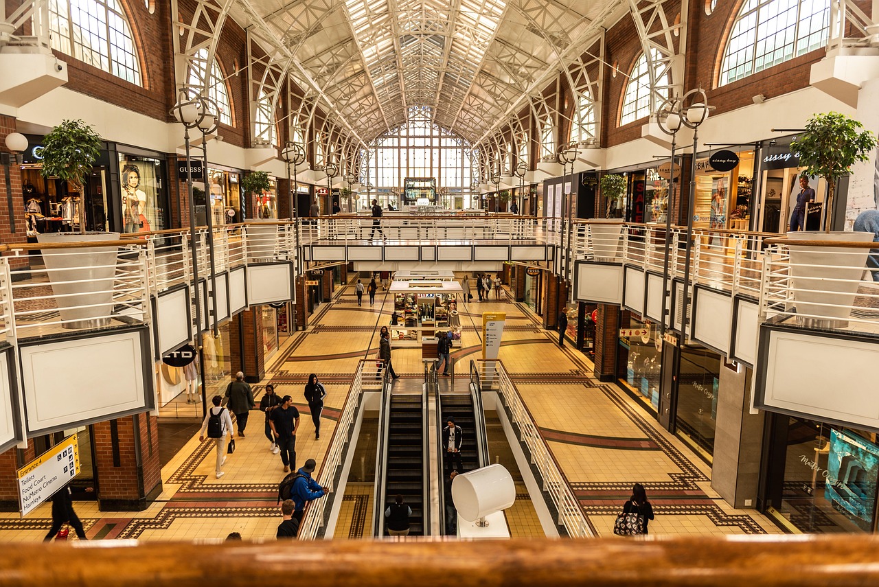 Vista interior de un centro comercial de varios niveles con personas caminando y escaleras mecánicas.