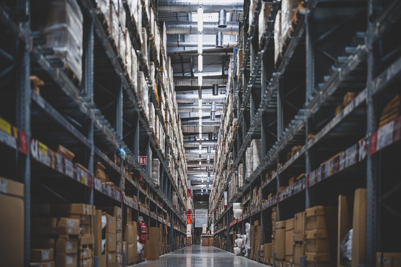 Pasillo central de un almacén industrial con estanterías metálicas de gran altura repletas de cajas de cartón.