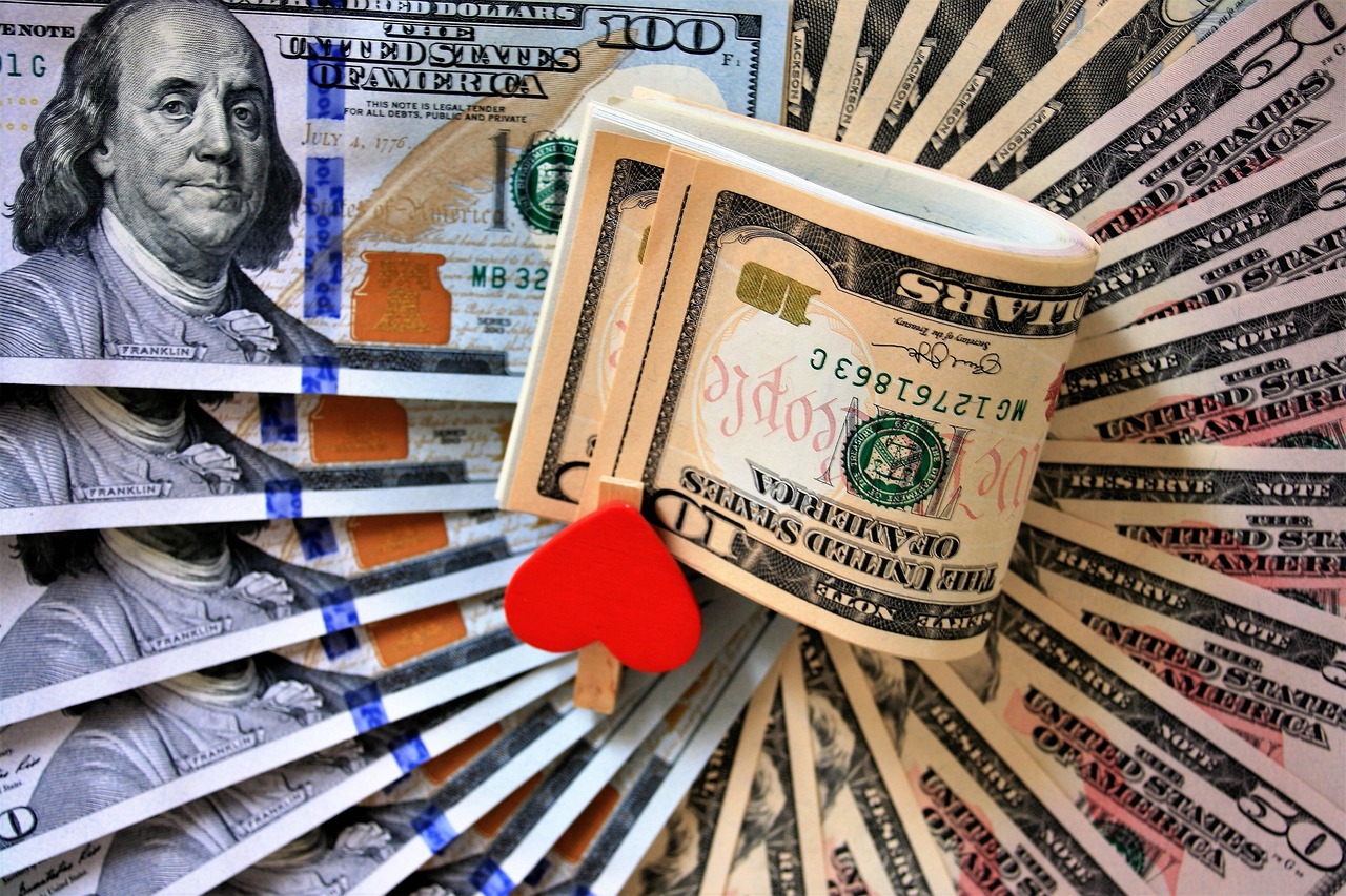 Una composición de billetes de dólares estadounidenses dispuestos en abanico con un pequeño clip en forma de corazón rojo sujetando un fajo central.